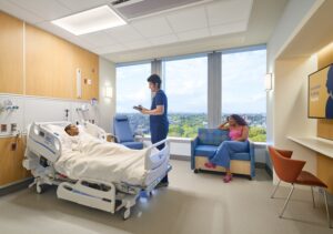 A room at Ruth Bader Ginsburg Hospital. A nurse is attending a patient. The wall of windows overlooks a scenic urban landscape.