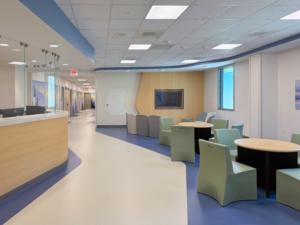 Hospital interior with sitting areas sat by tables and a lobby desk.