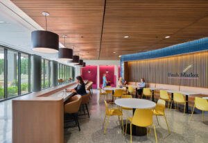 A sleek lounge with a bar table and booths. Colorful chairs fill the space and modern industrial lighting hangs from the ceiling.