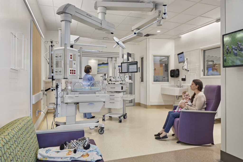 A NICU patient room accommodates both clinical practice and family presence with ceiling-mounted equipment arms that keep critical tools accessible while leaving room for a parent to stay close. 